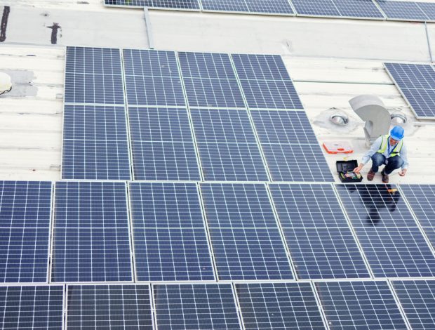 Solar panel, construction and industrial employees on roof for solar energy, engineering and sustainable lifestyle. Building, sustainability and teamwork for clean electricity and photovoltaic power.